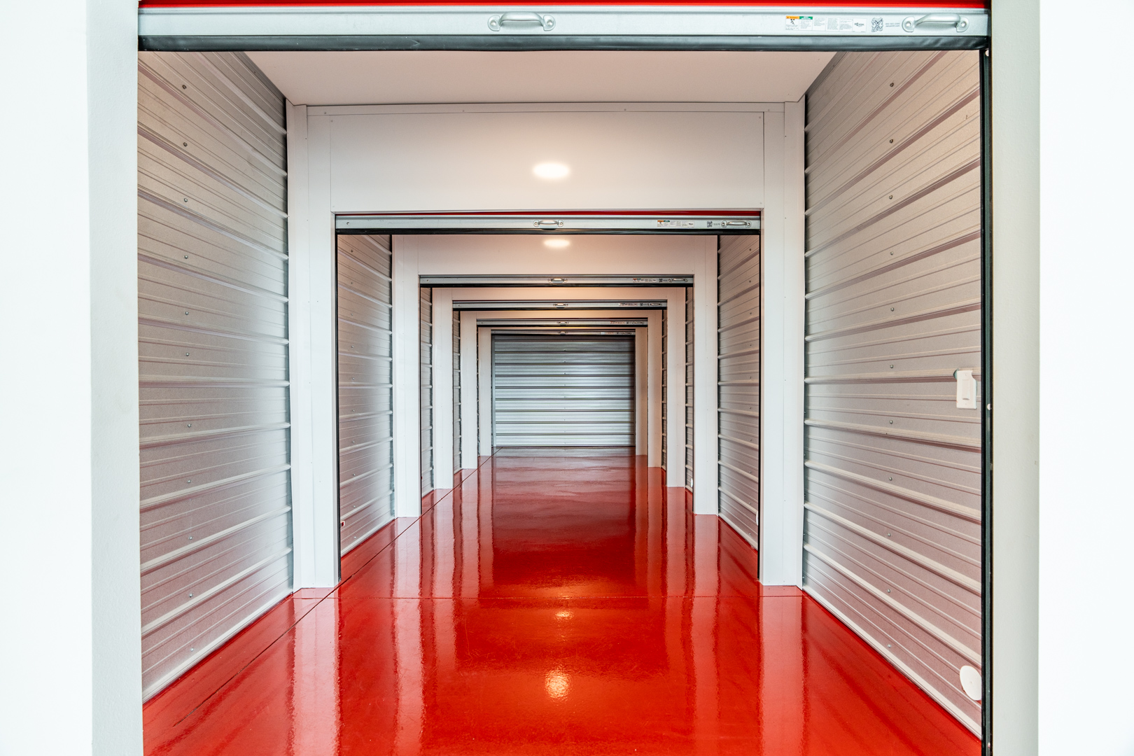 Storage Unit Hallway Interior | Modern Storage® Clean, well-lit storage unit hallway with red epoxy flooring and roll-up doors at Modern Storage® facility