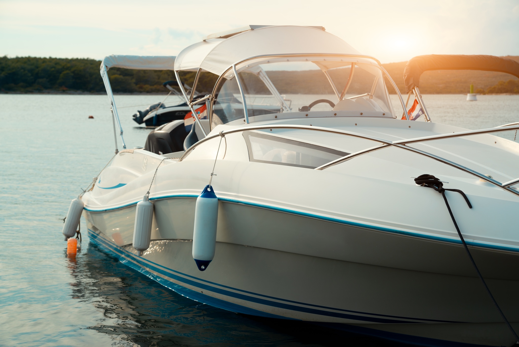 White boat on the water at sunset with bumpers hanging off the side.