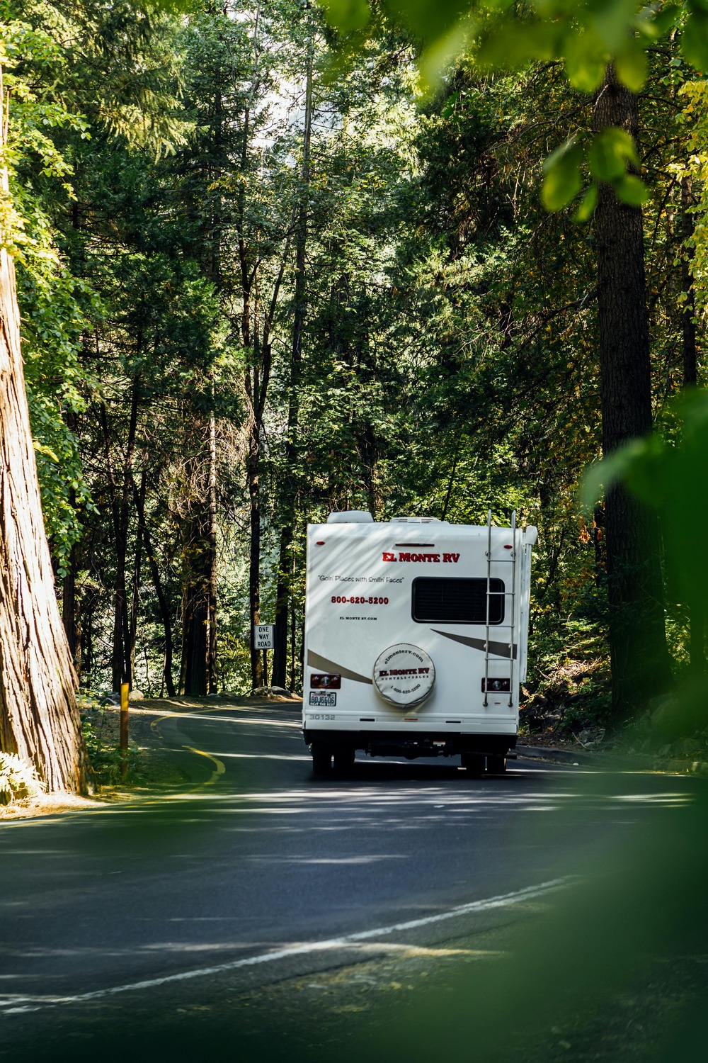 White rv driving down a road surrounded by trees