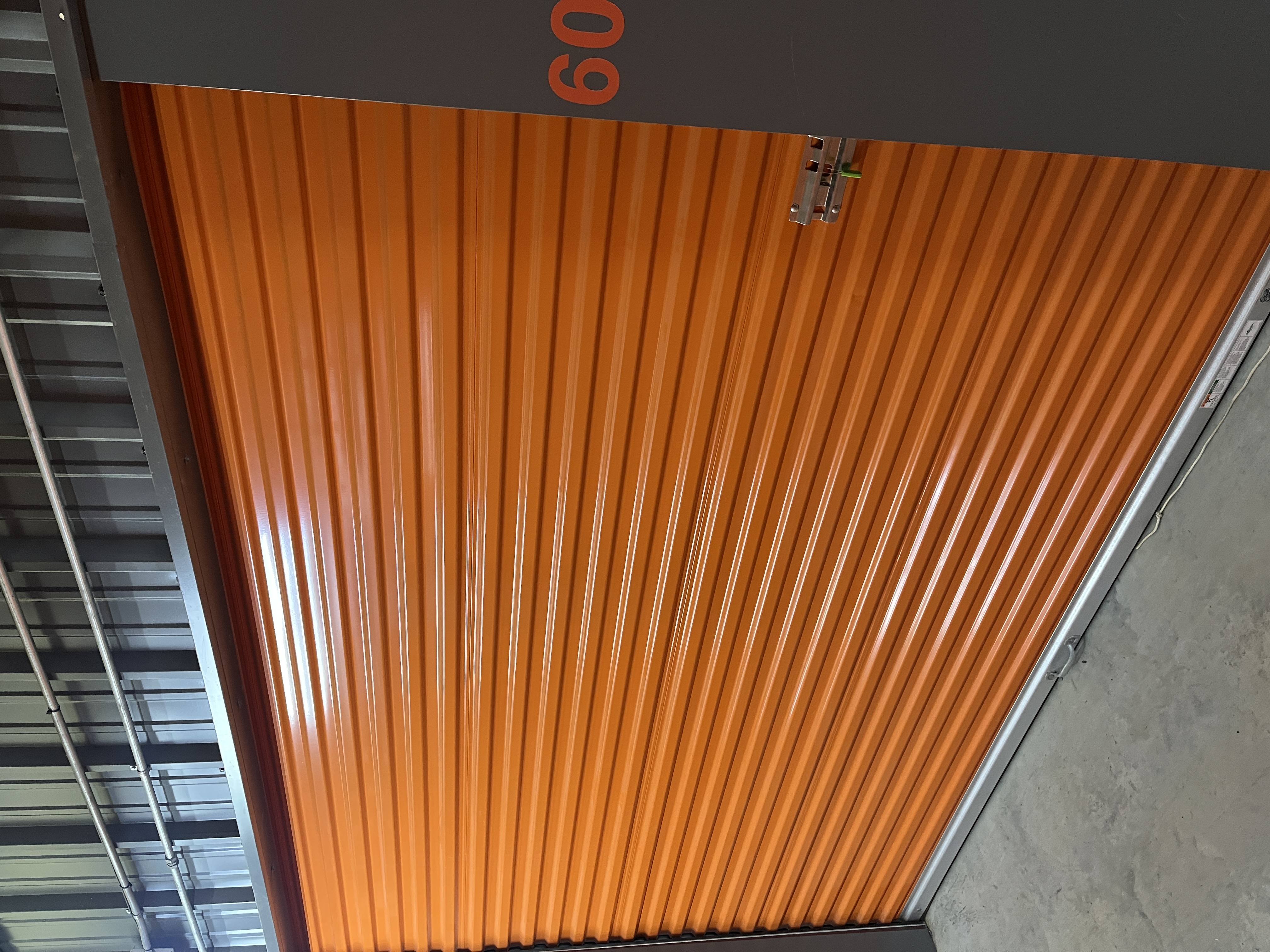 Closed orange roll-up door of a clean climate-controlled storage unit at Locked Up Storage in Greenwood, AR, with concrete flooring and secure locking hardware.