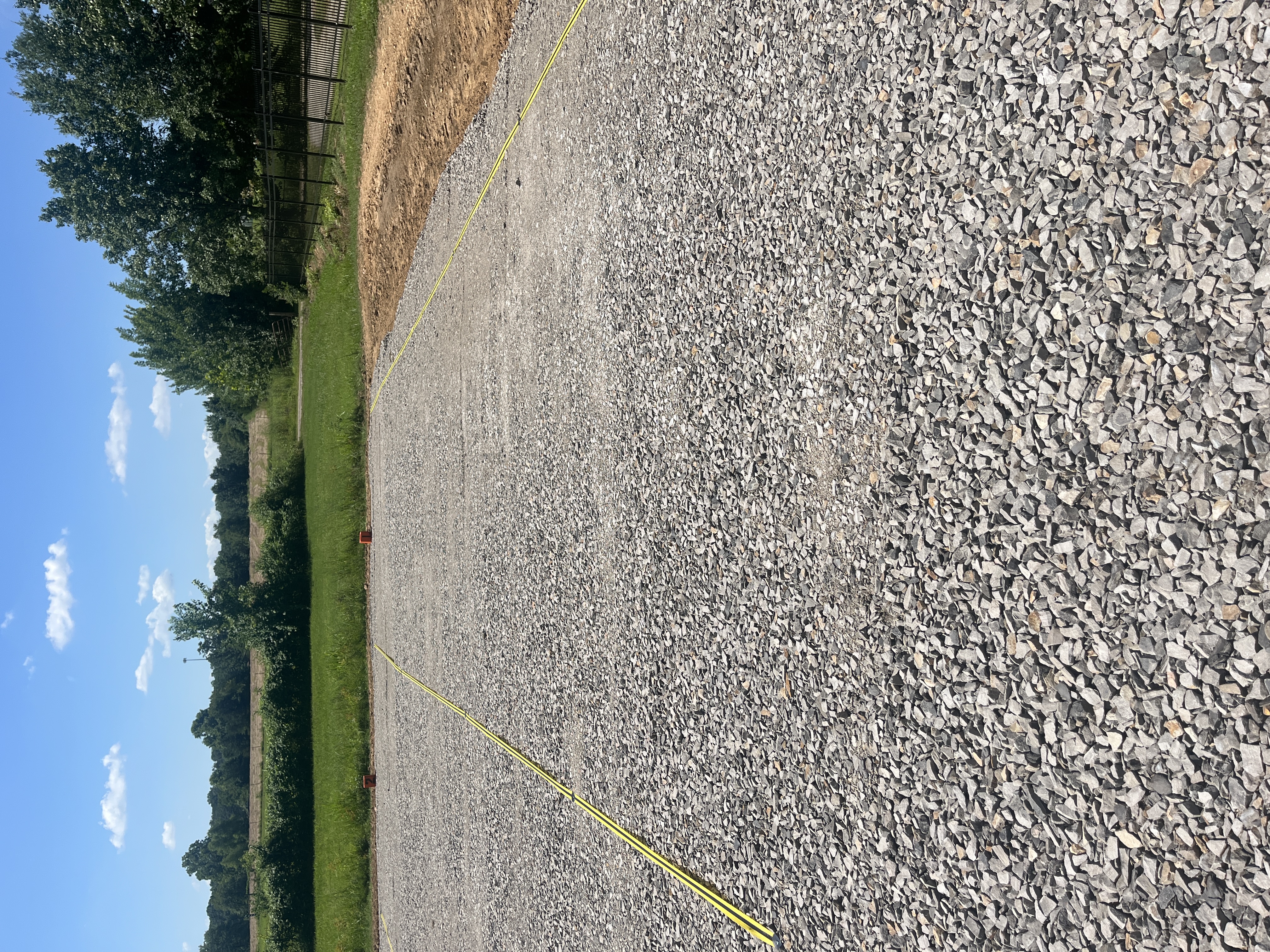 View of a freshly graveled parking section with yellow guide lines and open green field in the background.