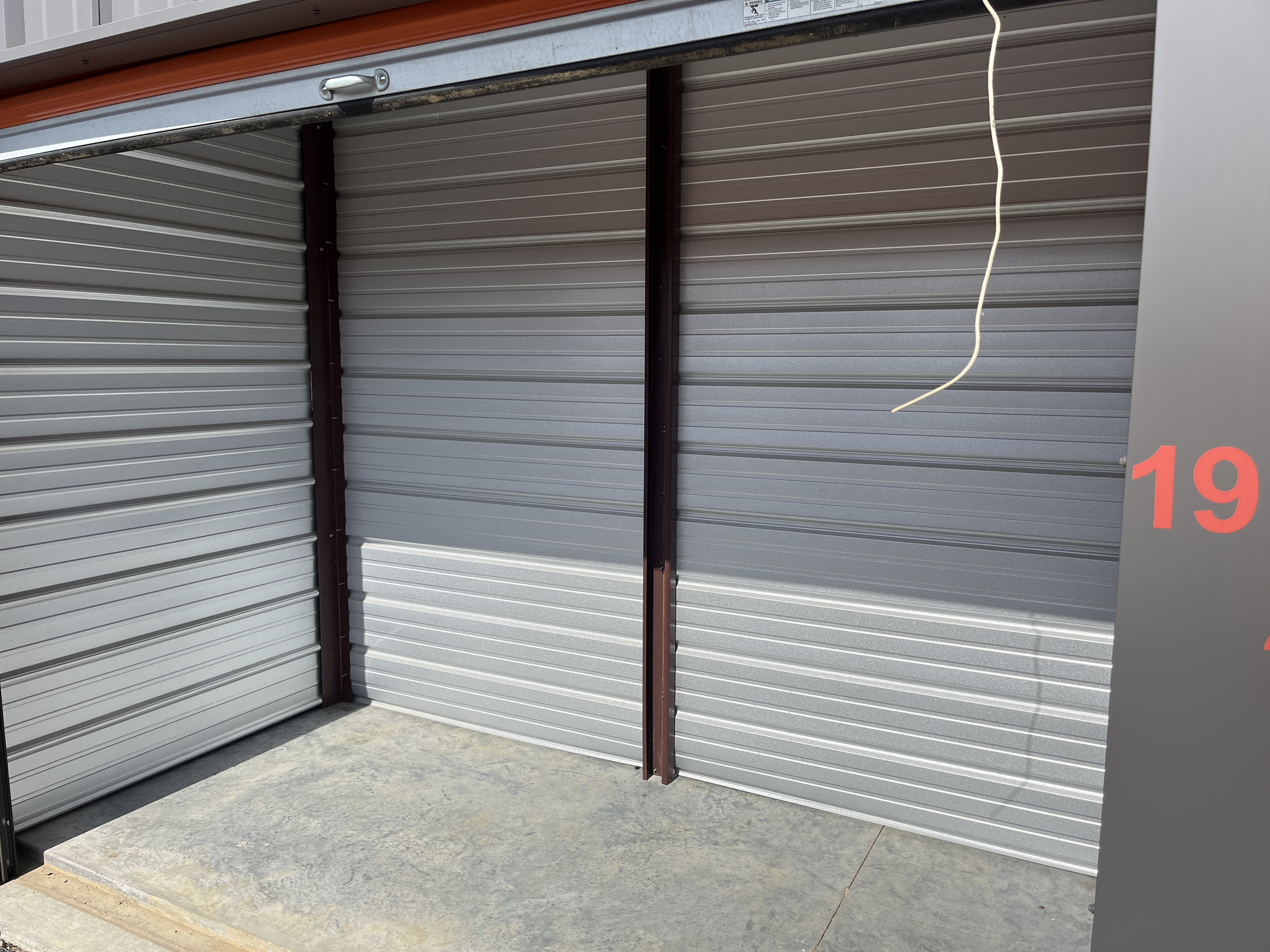 Open 10x10 non-climate-controlled storage unit at Locked Up Storage in Greenwood, AR, featuring clean metal interior walls, concrete flooring, and unit number 19 visible on the right panel.