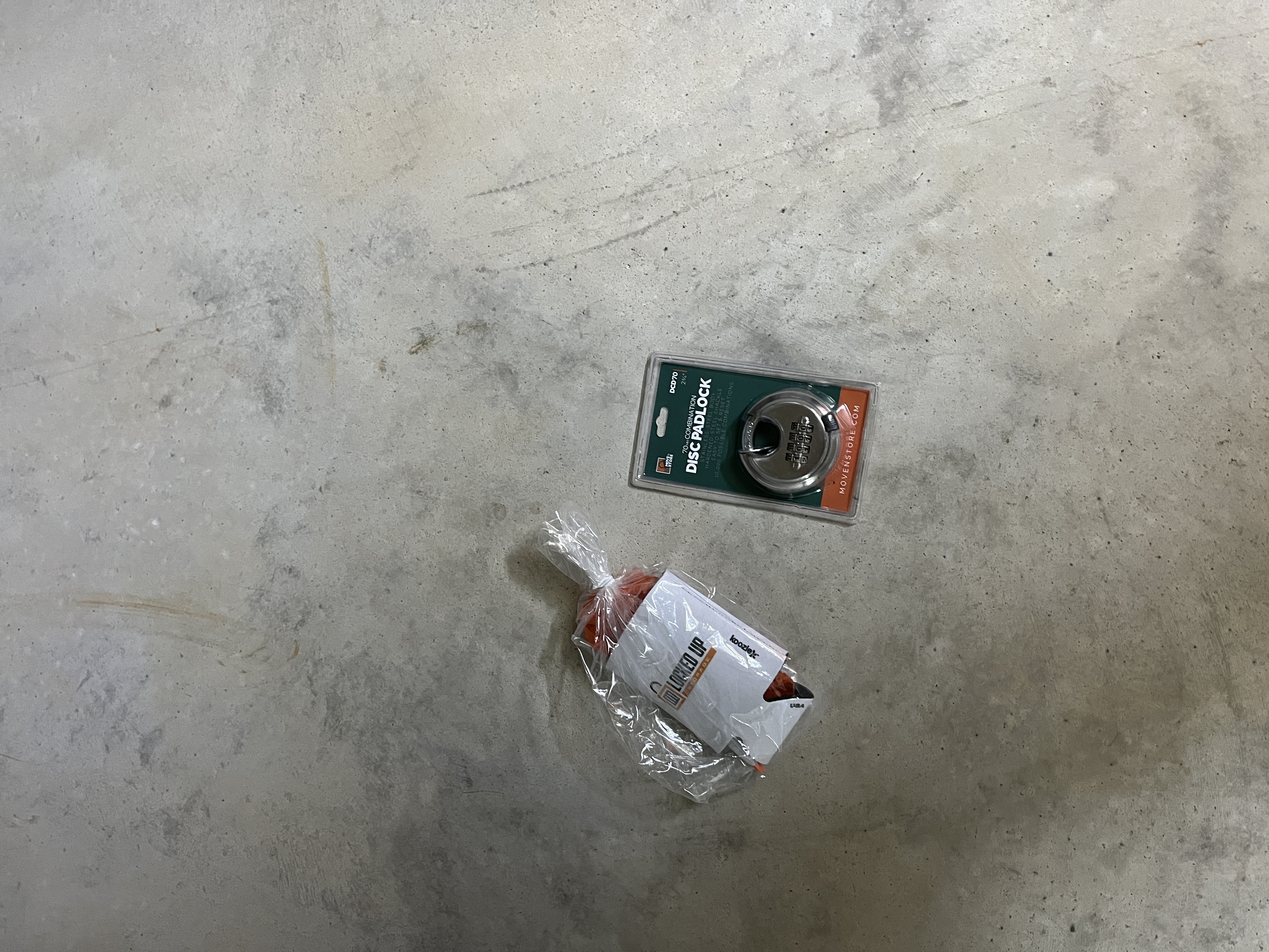 Free Combo Lock and Welcome Kit – Locked Up Storage Disc padlock and wrapped Locked Up Storage welcome packet resting on a concrete floor, ready for a new customer in Greenwood, AR.