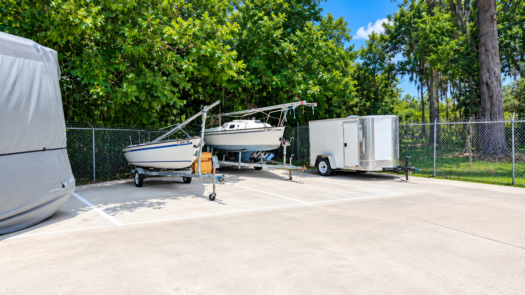 Boats and a trailer parked in gated outdoor spaces at Ocala Storage Park