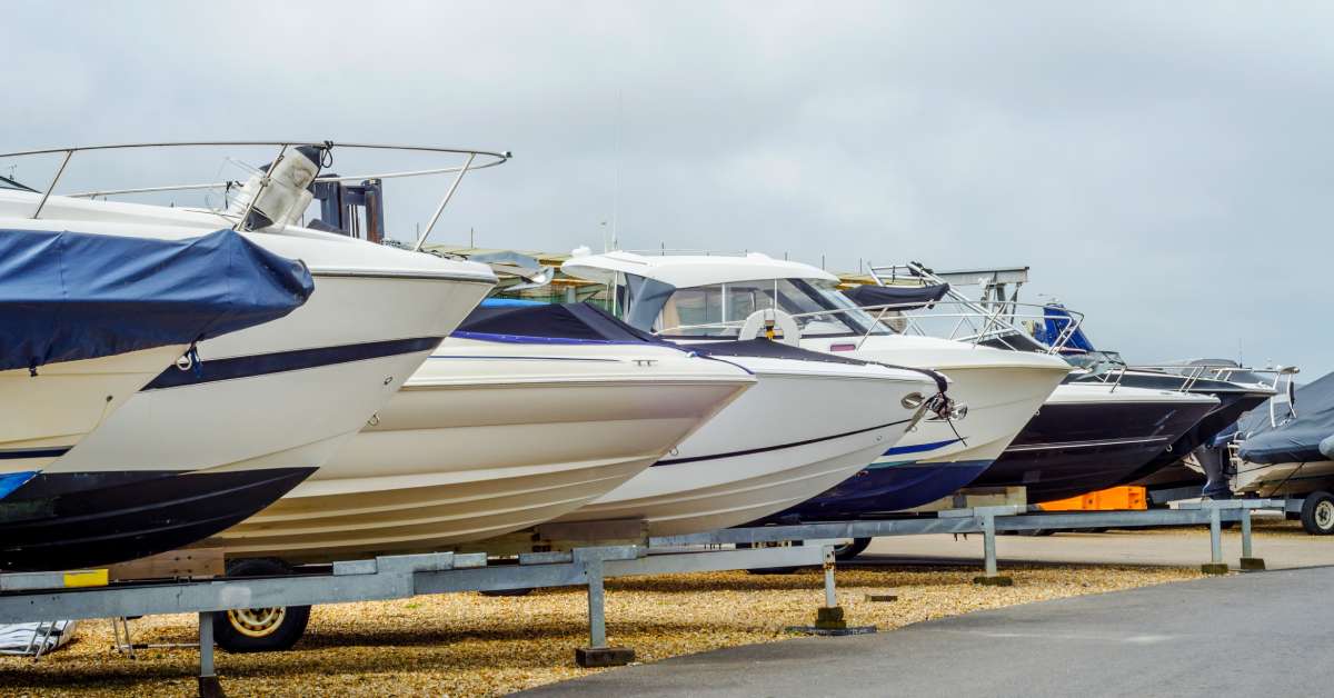 A closeup of several different color boats in trailers lined up next to each other in a storage facility parking lot.