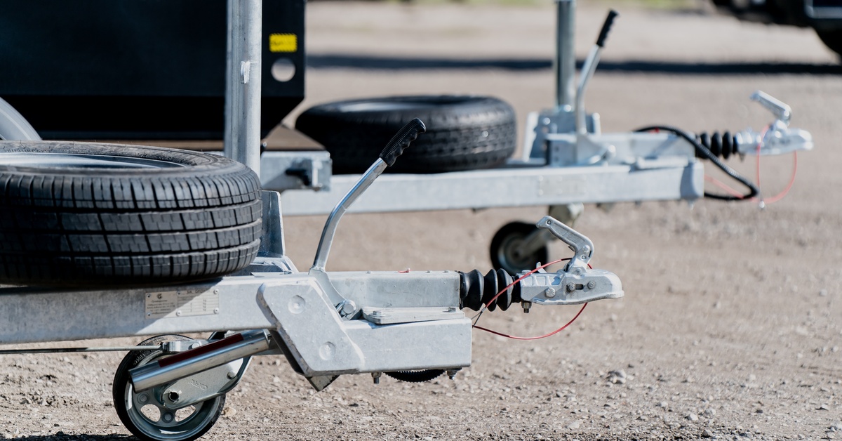 The hitch end of two trailers. They both have spare tires attached to them and are parked in a gravel parking lot.
