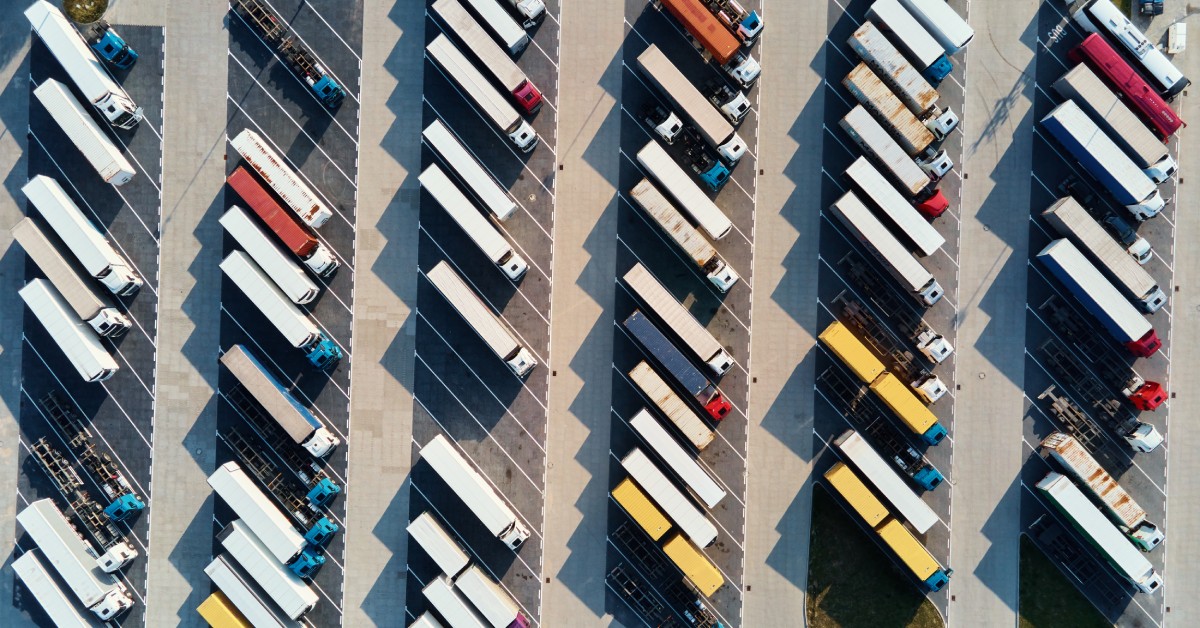 The Benefits of On-Demand Parking for Independent Truckers An aerial view of a semi-truck parking lot. Most of the spaces are filled, but there are a few empty ones spread throughout.