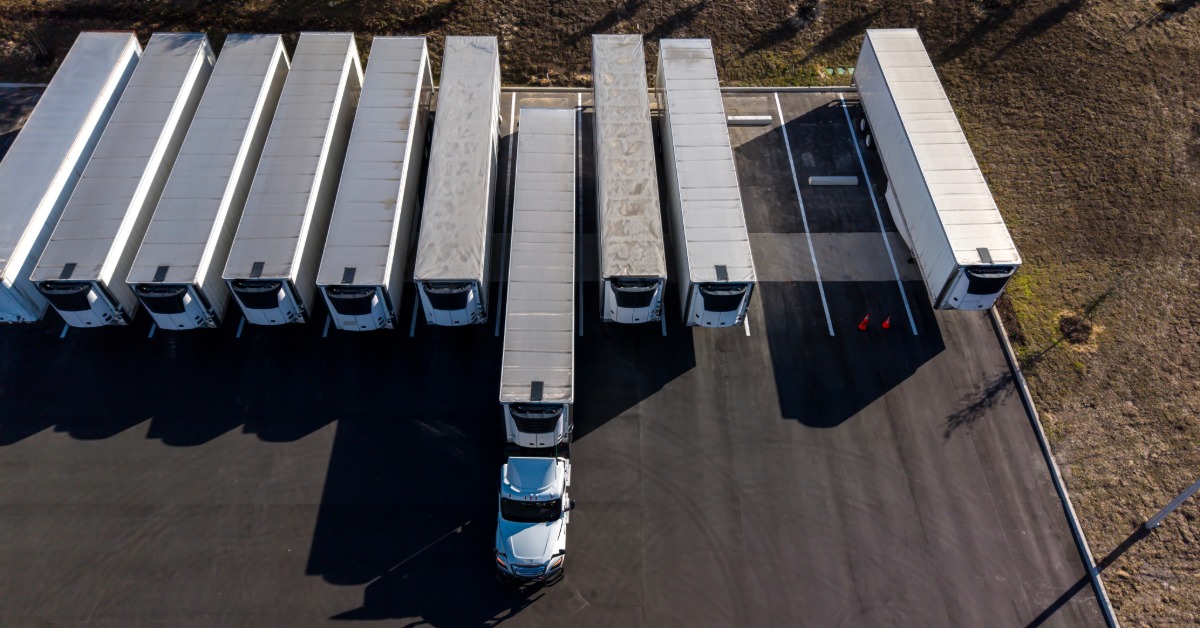 A semi truck backing into a spot surrounded by other trailers. All the other trailers are perfectly aligned with each other.