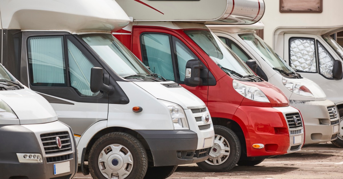Multiple camper vans parked in a paved lot. One of the campers is red, but the rest of them are white.