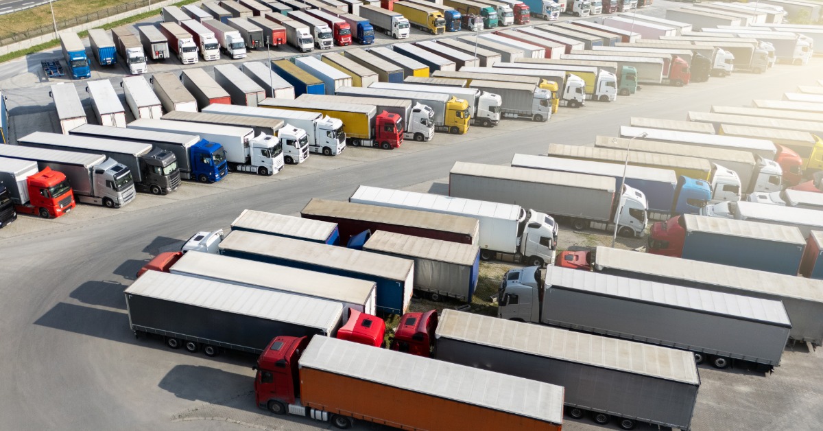 An aerial view of a large truck trailer parking lot with multiple rows of semi-trucks with trailers parked together.