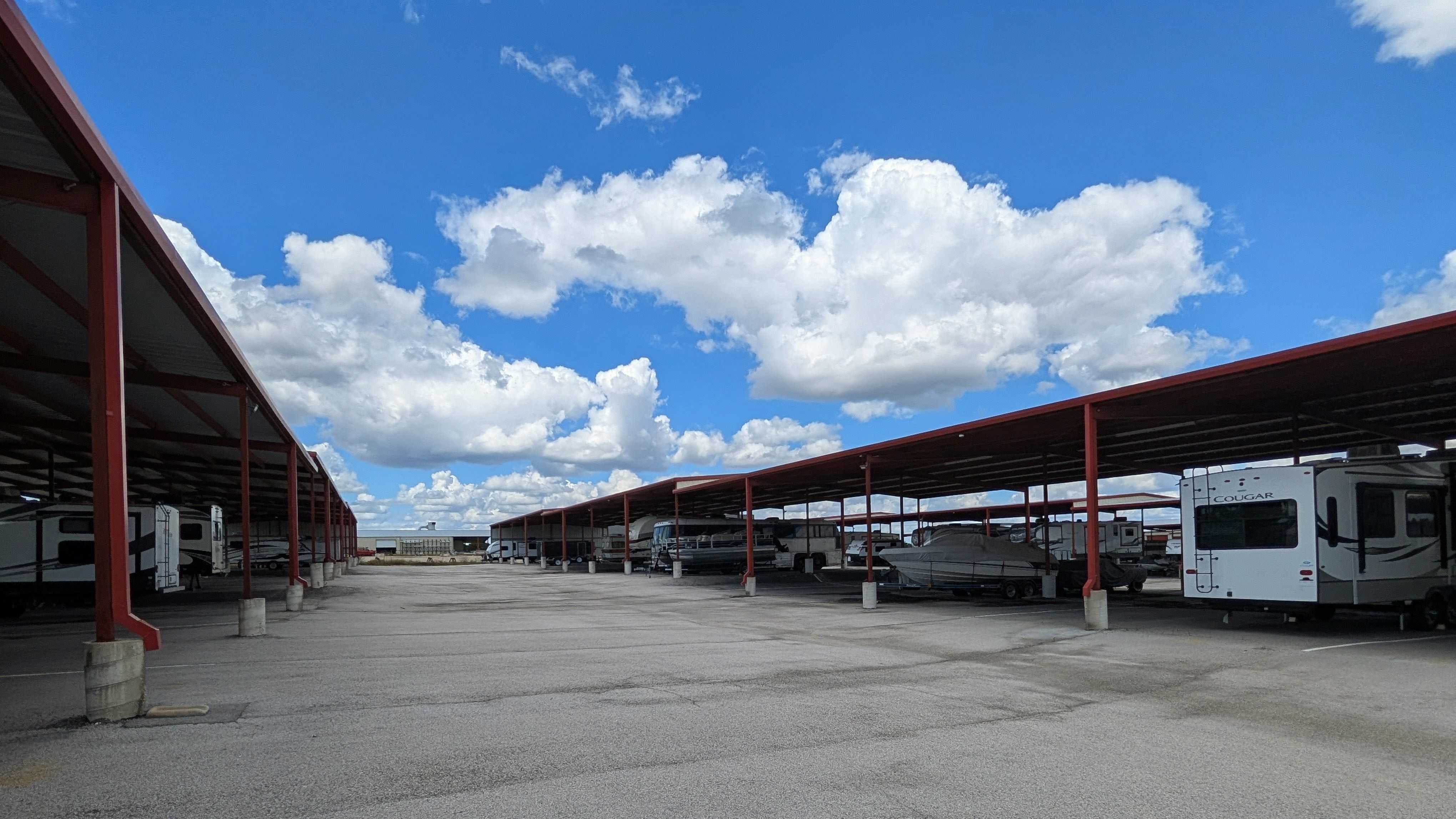 Long drive aisle between two rows of covered parking stalls, storing multiple RVs, trailers, and a boat.
