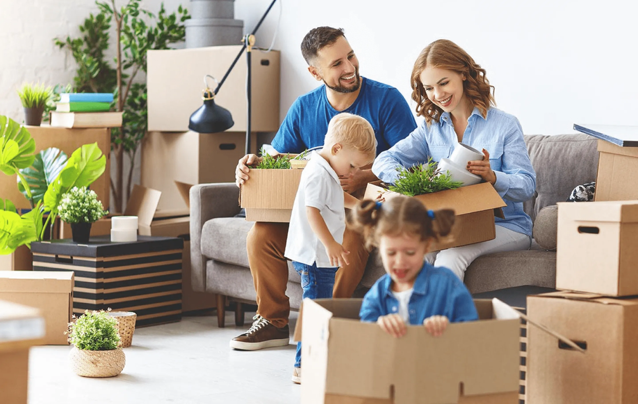A happy family with two young children packing cardboard boxes and house plants in their Caddo Mills, TX home to prepare for a move.