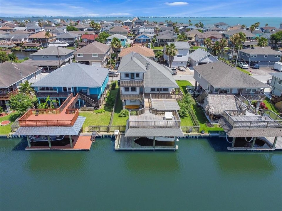 An aerial perspective of coastal residential homes in Bayou Vista, Texas, featuring multi-story houses with private boat lifts and wooden decks along a calm canal leading to the open bay.