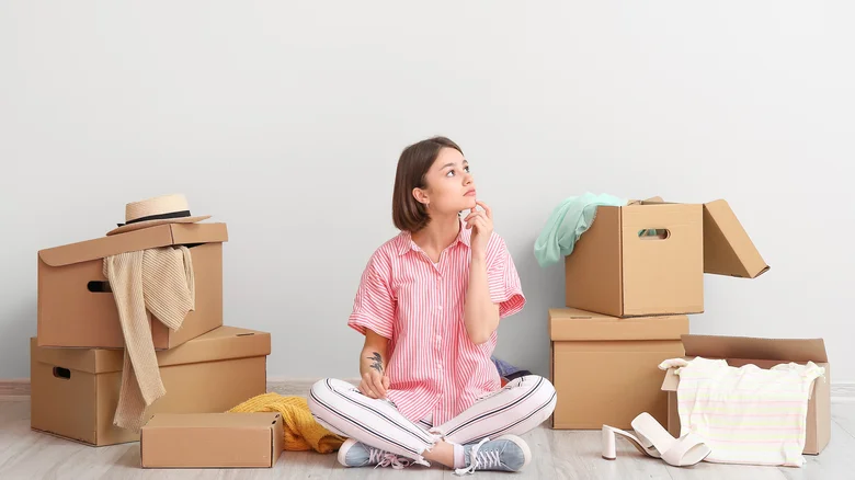 A woman sitting among packed moving boxes, thoughtfully considering storage facility security features near Galveston, TX.