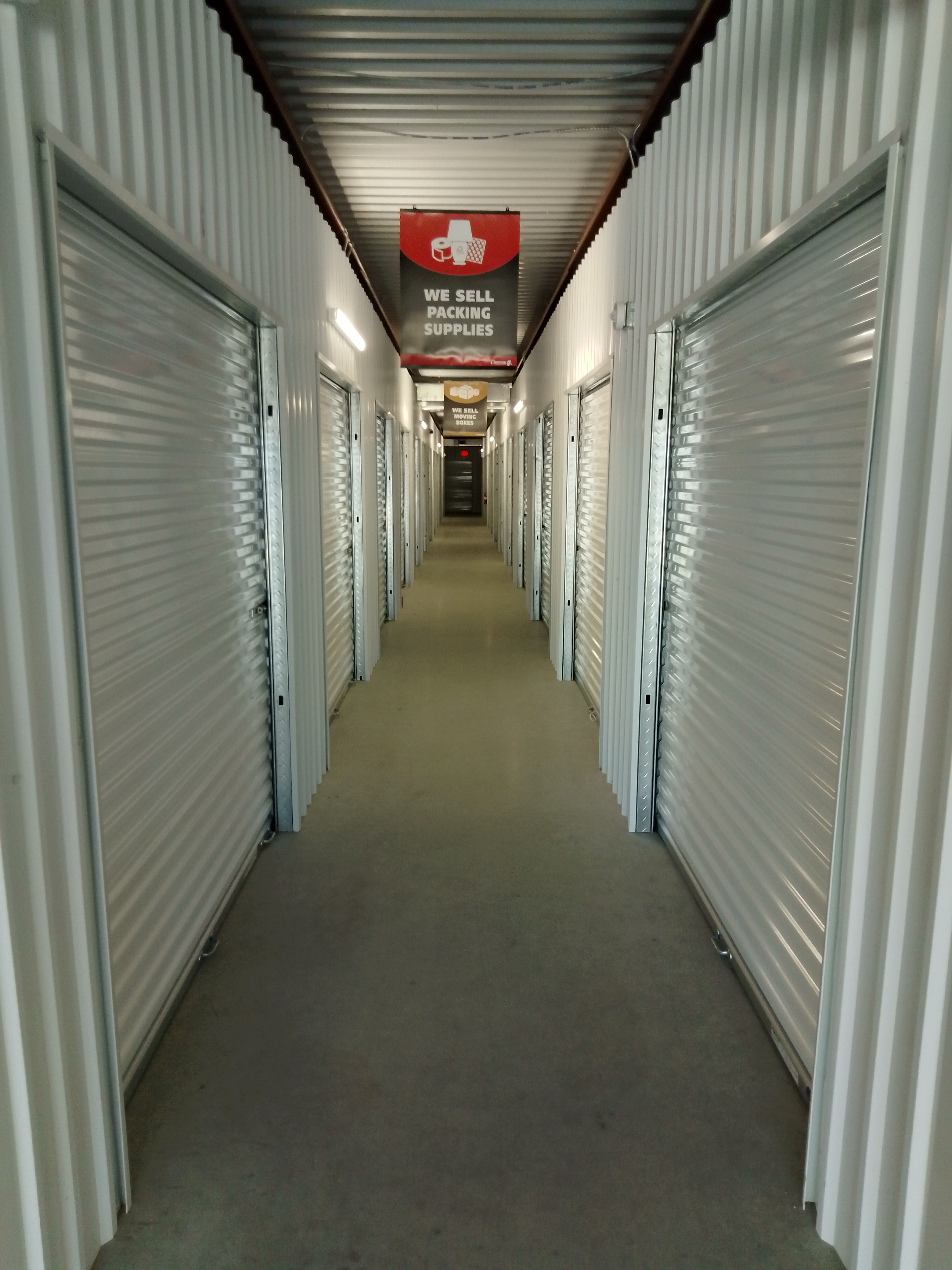 Interior hallway of climate-controlled self-storage units with roll-up doors and signage for packing supplies at Spicewood Super Storage in Texas.