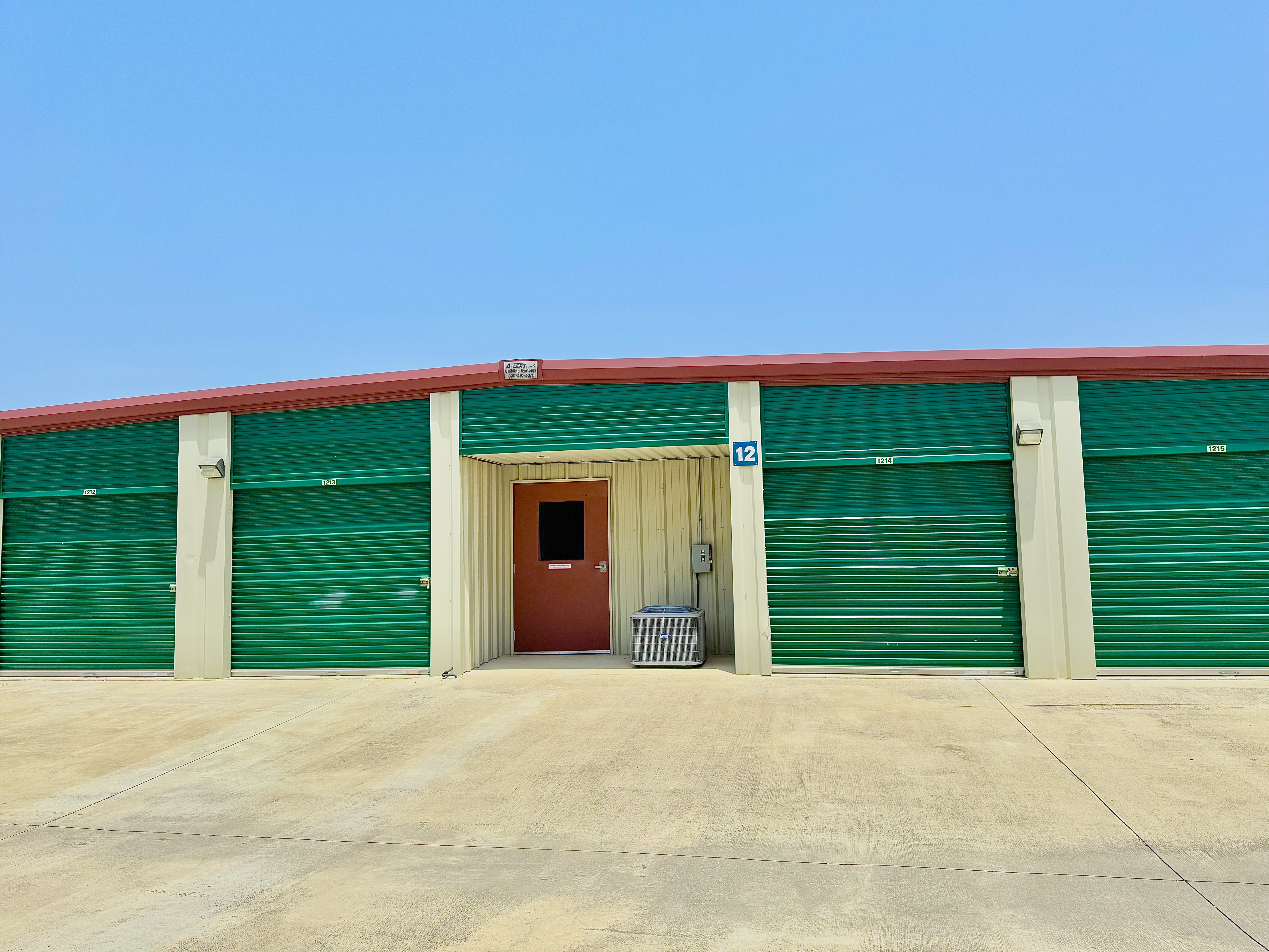 Climate-controlled self storage building with green roll-up doors and a red access door at LockSmart Climate Storage near Luling, TX