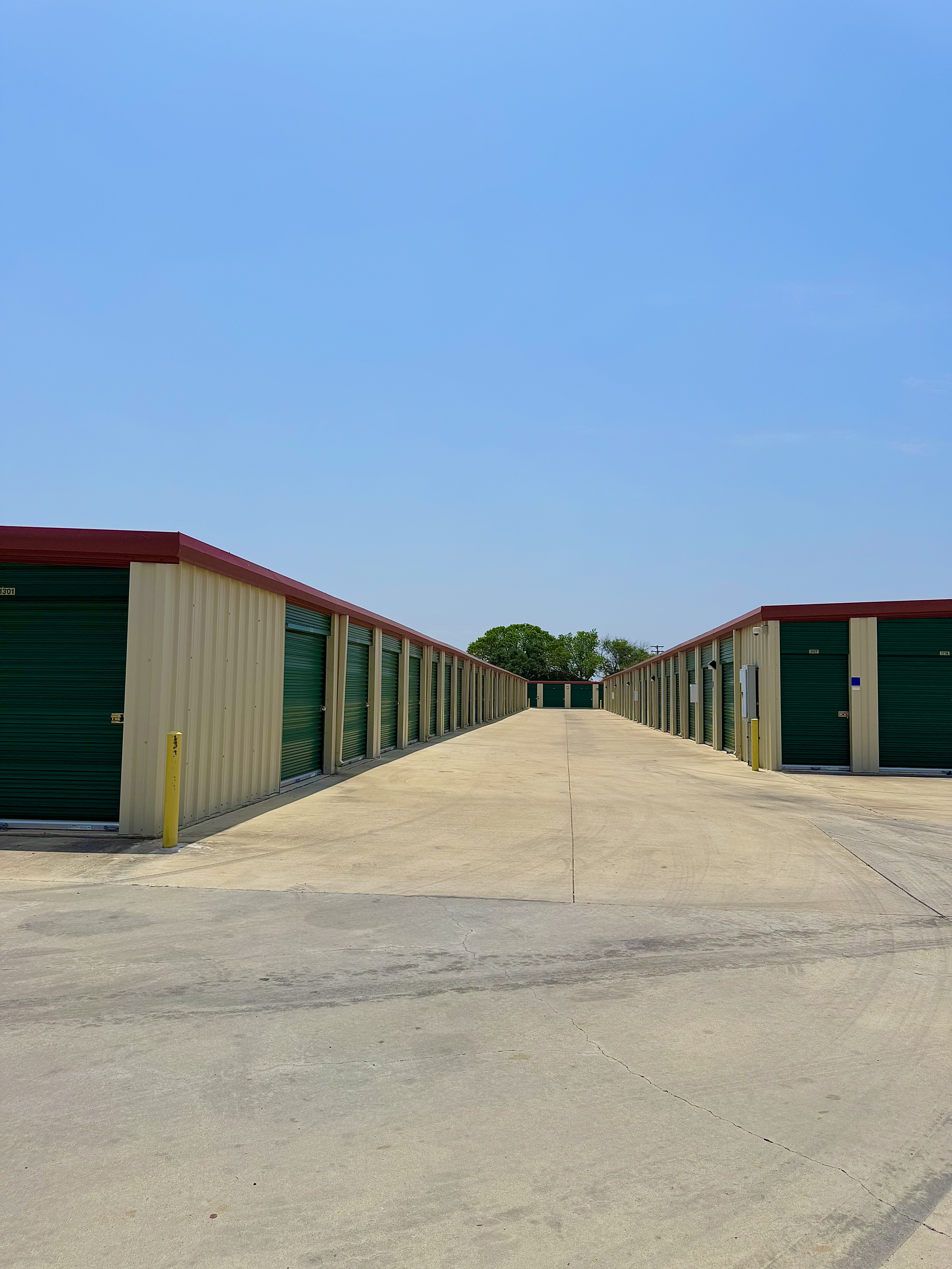 Outdoor drive-up self storage units with green doors and red roofs under a clear blue sky at LockSmart Climate Storage in Lockhart, TX.
