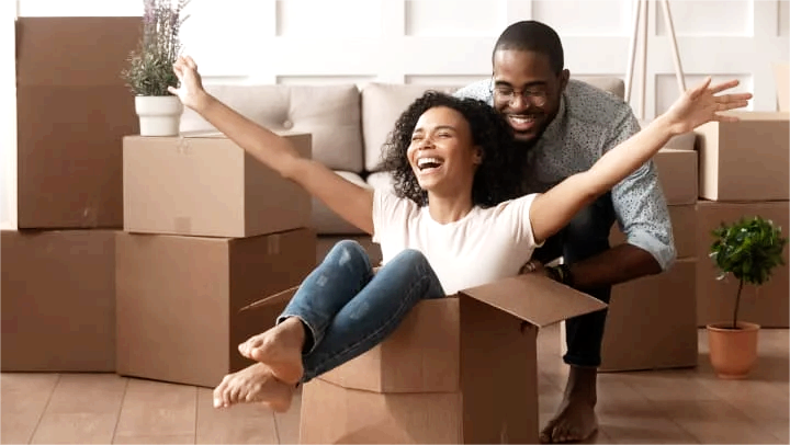 A happy couple playing with cardboard moving boxes in their living room, illustrating the joy of finding extra space with storage units in Royse City. Why Families Near Royse City, TX Rely on Storage Units for Extra Space