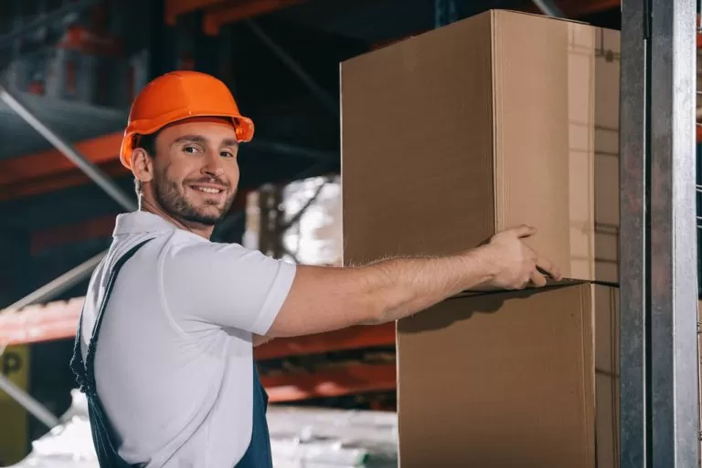 A friendly onsite manager wearing a hard hat and smiling while assisting with storage boxes at a Royse City facility. The Value of Onsite Storage Managers in Royse City, TX