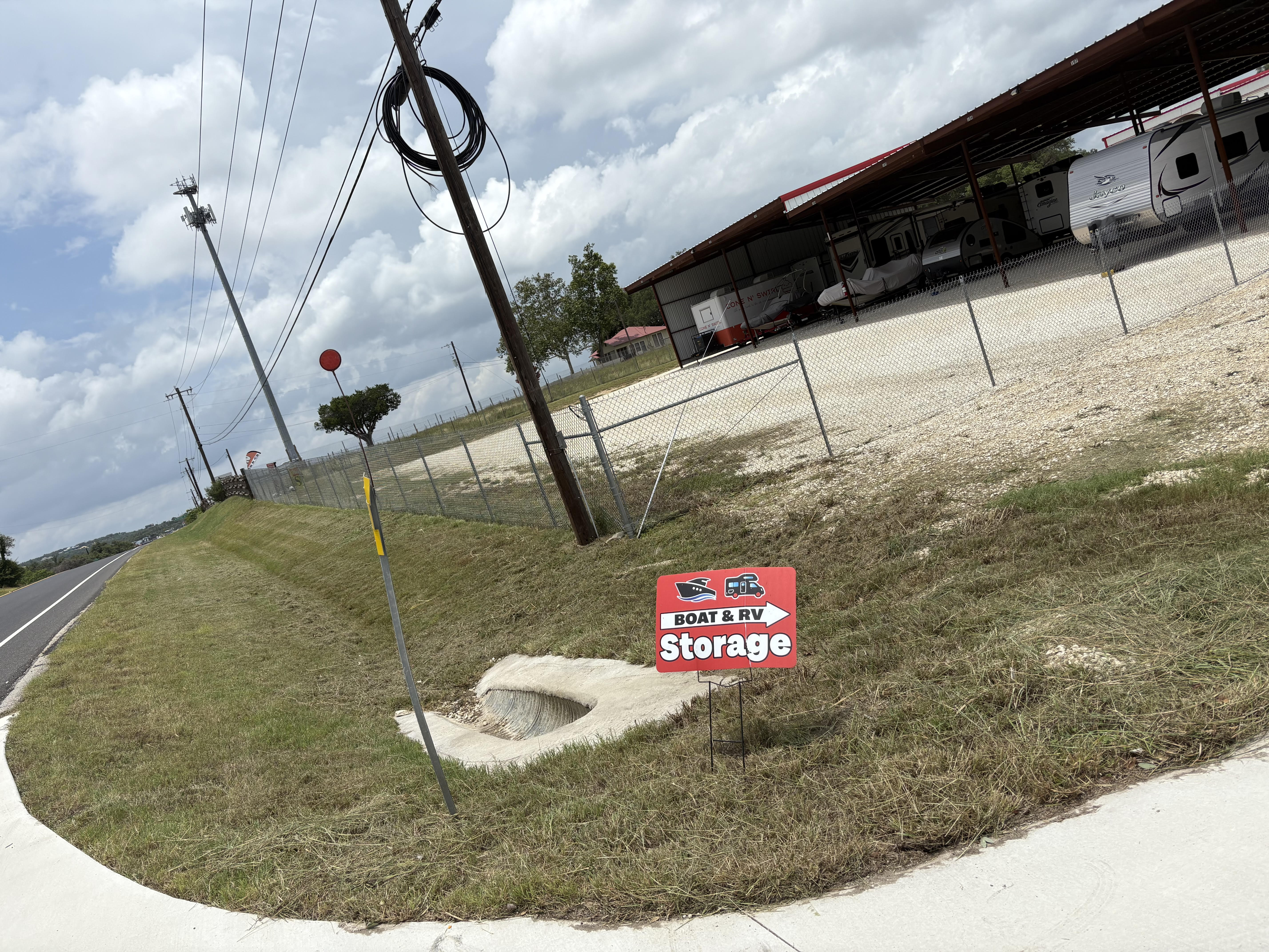 Secure Covered Boat and RV Storage Facility in Boerne Texas Covered boat and RV storage facility near Boerne, TX with gravel lot, fenced security, and directional signage