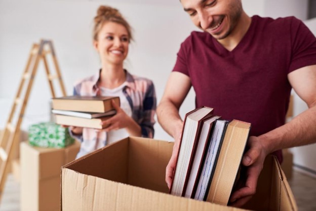 Downsizing Homes with Storage Units in Spicewood, TX A woman smiling while packing a large cardboard box in a Spicewood, TX home to prepare for a downsizing move.