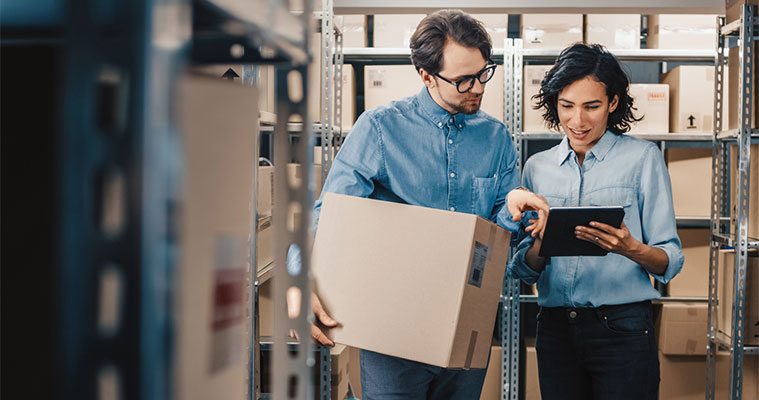 Choosing the Right Storage Unit Size in Spicewood, TX A man and woman in a Spicewood, TX storage facility using a digital tablet to calculate the correct unit size for their boxes.