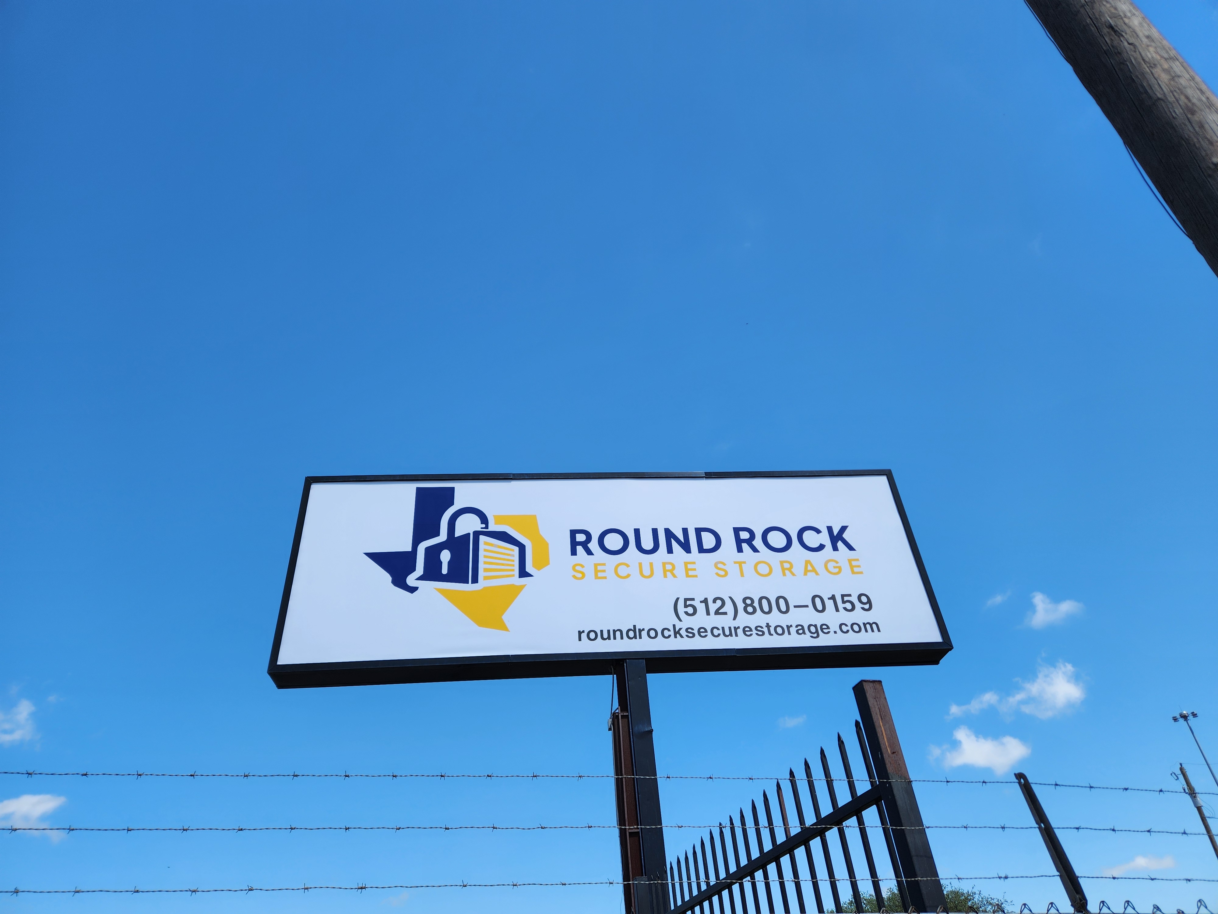 Round Rock Secure Storage facility sign with logo, phone number, and website against a clear blue Texas sky.
