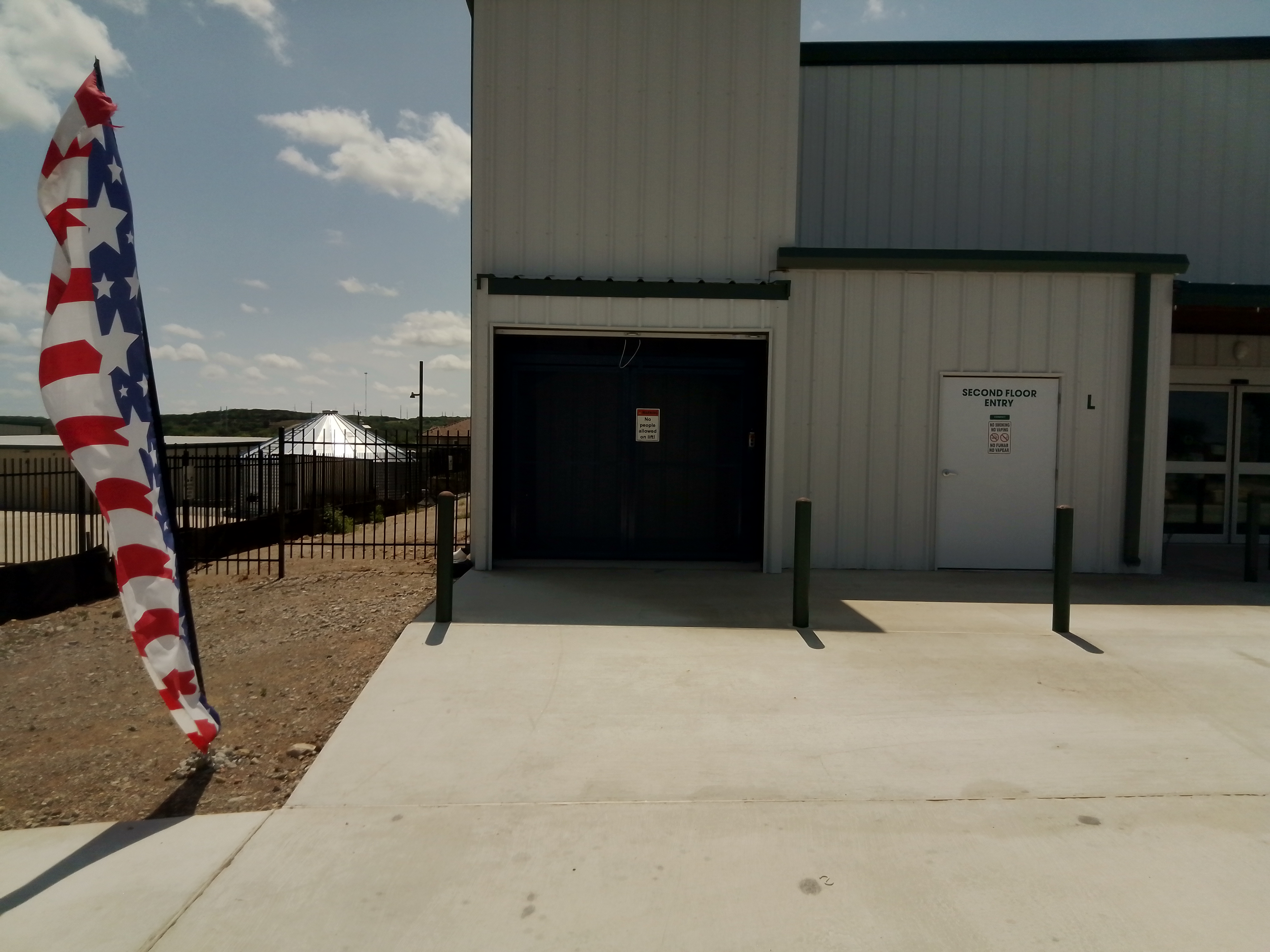 Ground-level entry and elevator access point at Spicewood Super Storage near Bee Cave, TX, with secure fencing and patriotic flag signage.