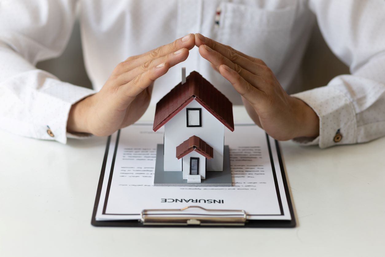 Two hands covering a model house on top of an insurance quote