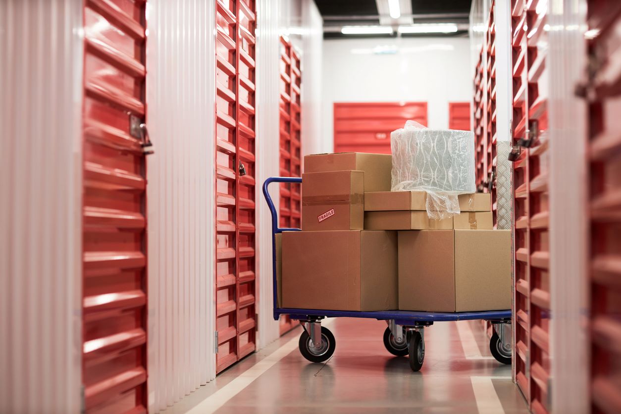 A cart piled high with boxes sits in a storage facility surrounded by red units.