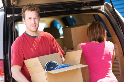 Couple unloading car, man holding box with items inside, woman facing into the car