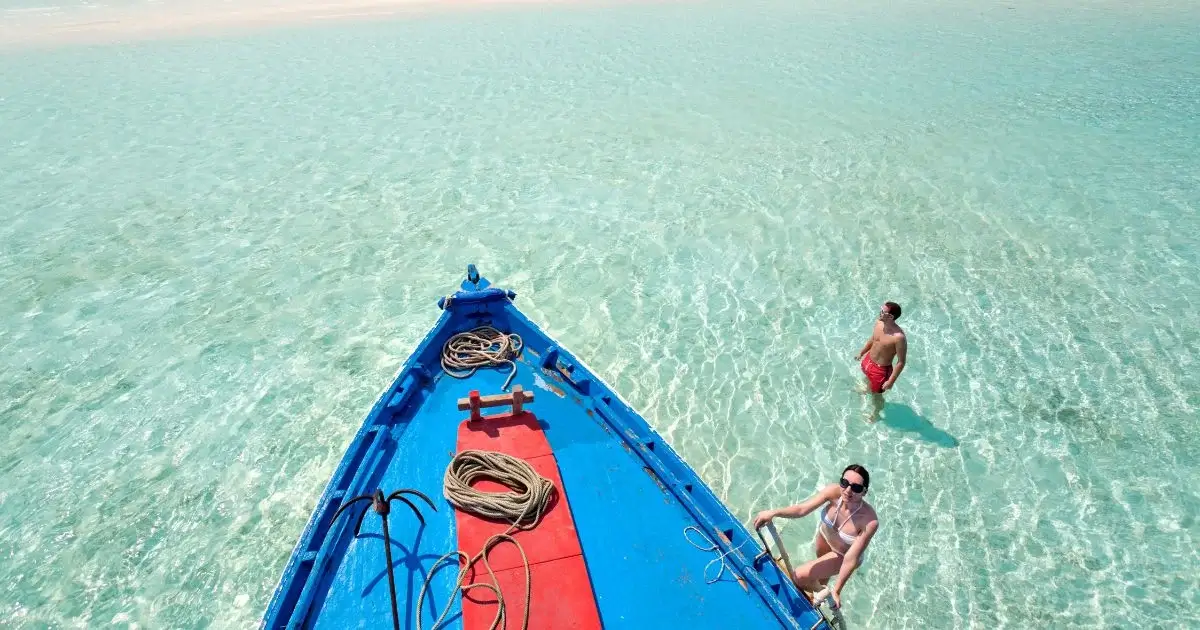 People near boat in clear shallow tropical water.