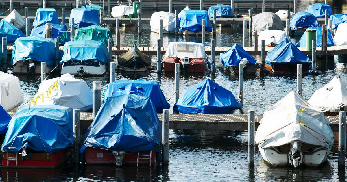 Boats covered with blue and white tarps docked in a marina for storage.