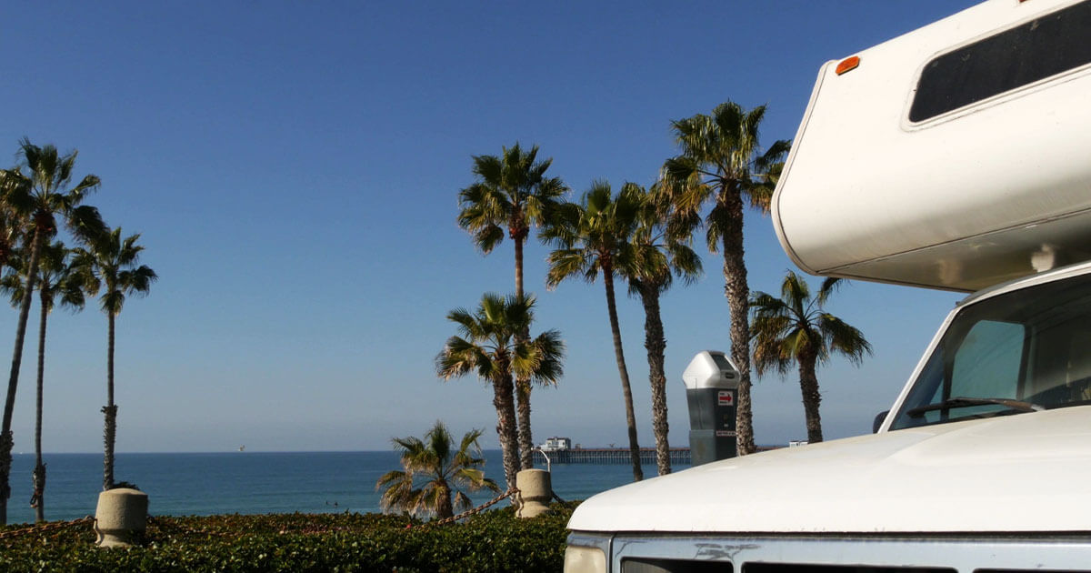 RV parked at a scenic beachside location with a picnic table and chairs set up near the ocean.