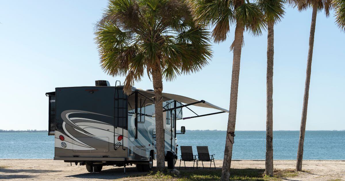 RV camper parked by beach with palm trees