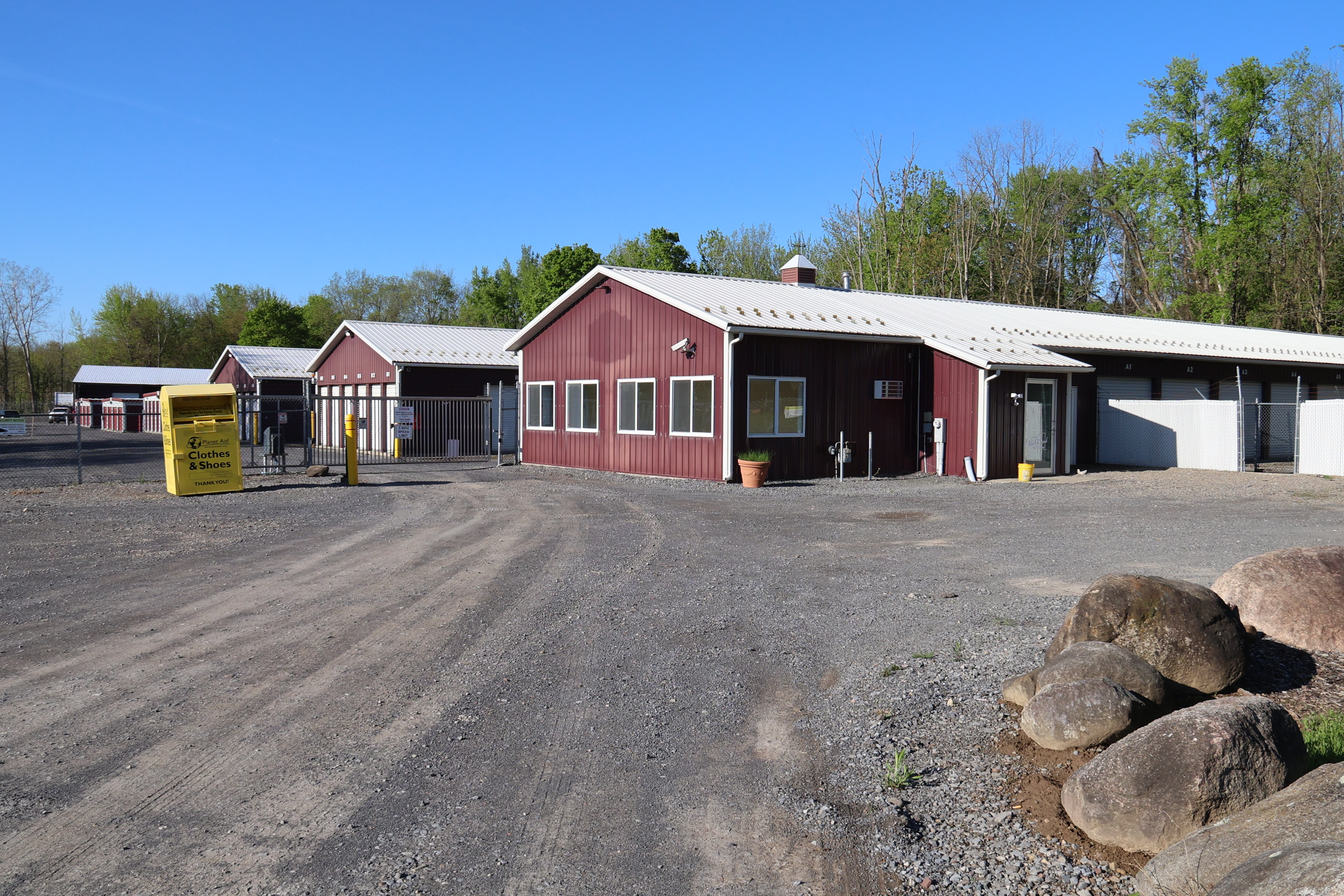 A-Verdi Self Storage Syracuse office building with red metal exterior, white trim, and gravel lot at the entrance