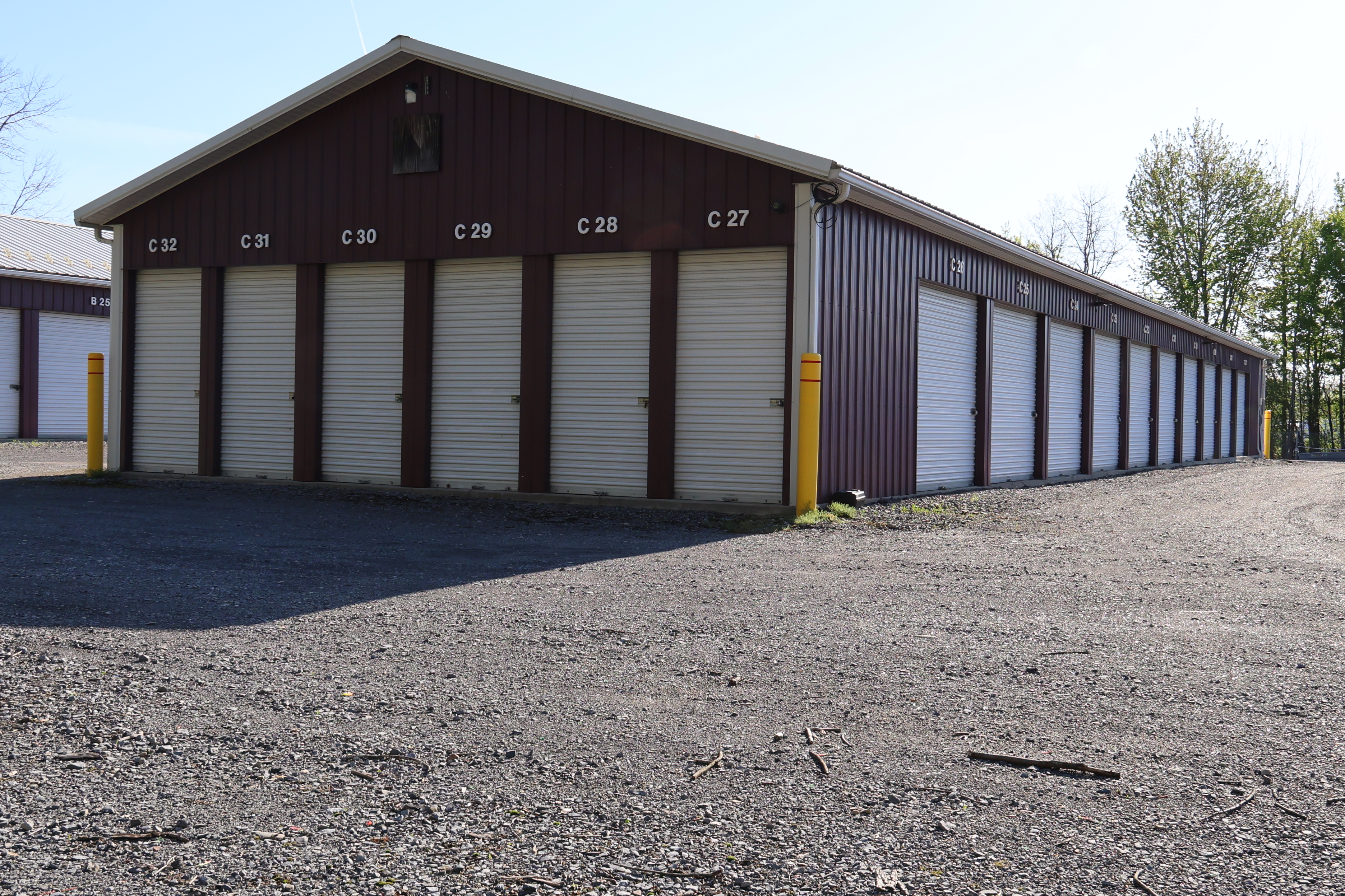 Drive-up storage units at A-Verdi Self Storage Syracuse with white roll-up doors, unit numbers, and wide gravel access