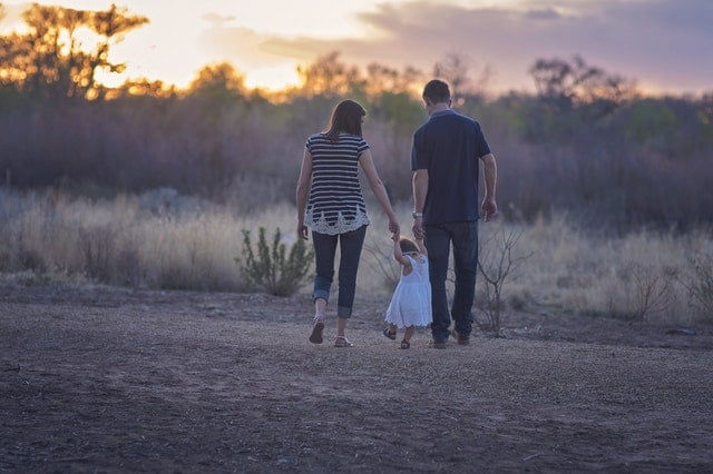 Two adults holding their child's hands as they walk in a desert scene