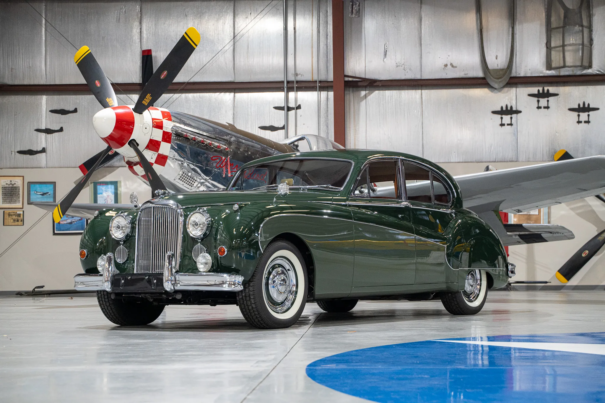 1961 Jaguar Mark IX Displayed in Aircraft Hangar Front three-quarter view of a classic 1961 Jaguar Mark IX displayed indoors with a vintage propeller aircraft in the background