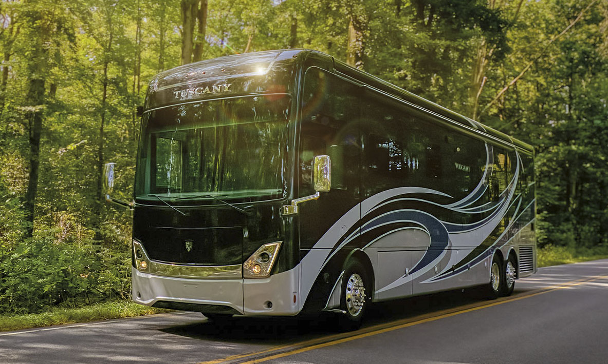 Luxury Thor Motor Coach Tuscany Class A diesel motorhome in black and silver driving on a tree-lined road, showcasing full-body paint, chrome accents, and modern aerodynamic styling