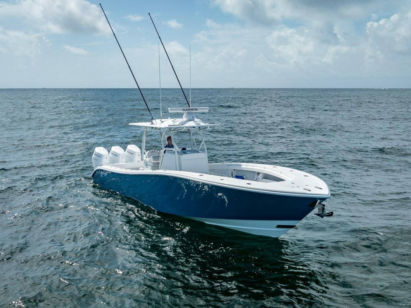 Blue and white luxury center console sportfishing yacht with quad Yamaha outboard engines, hardtop tower with outriggers, and Garmin radar cruising on calm open water
