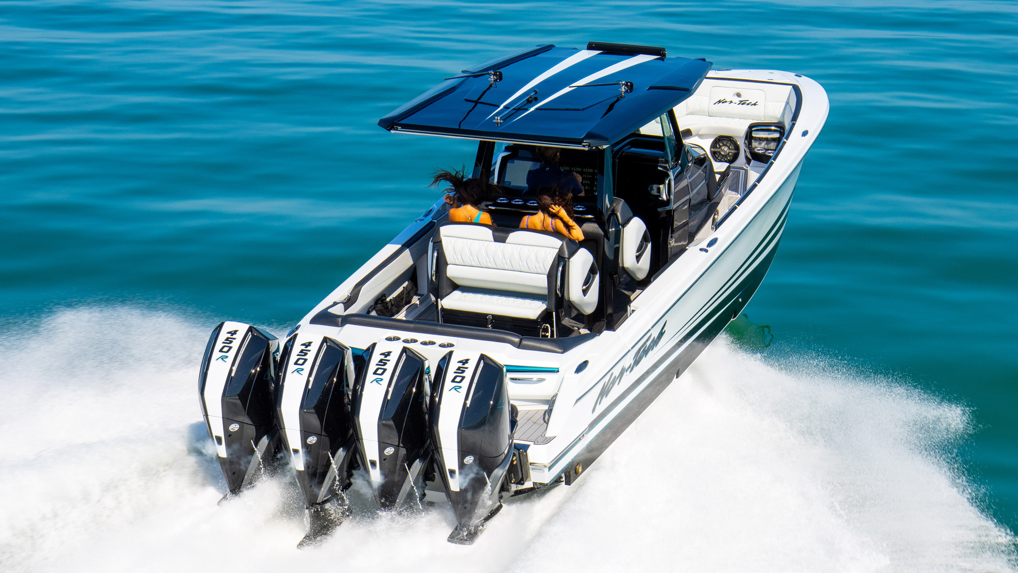 Exhilaration like this deserves concierge-level protection on land. High-performance Nor-Tech center console luxury powerboat with quadruple Mercury 450R outboard engines speeding across turquoise water, featuring extended hardtop shade and premium seating.