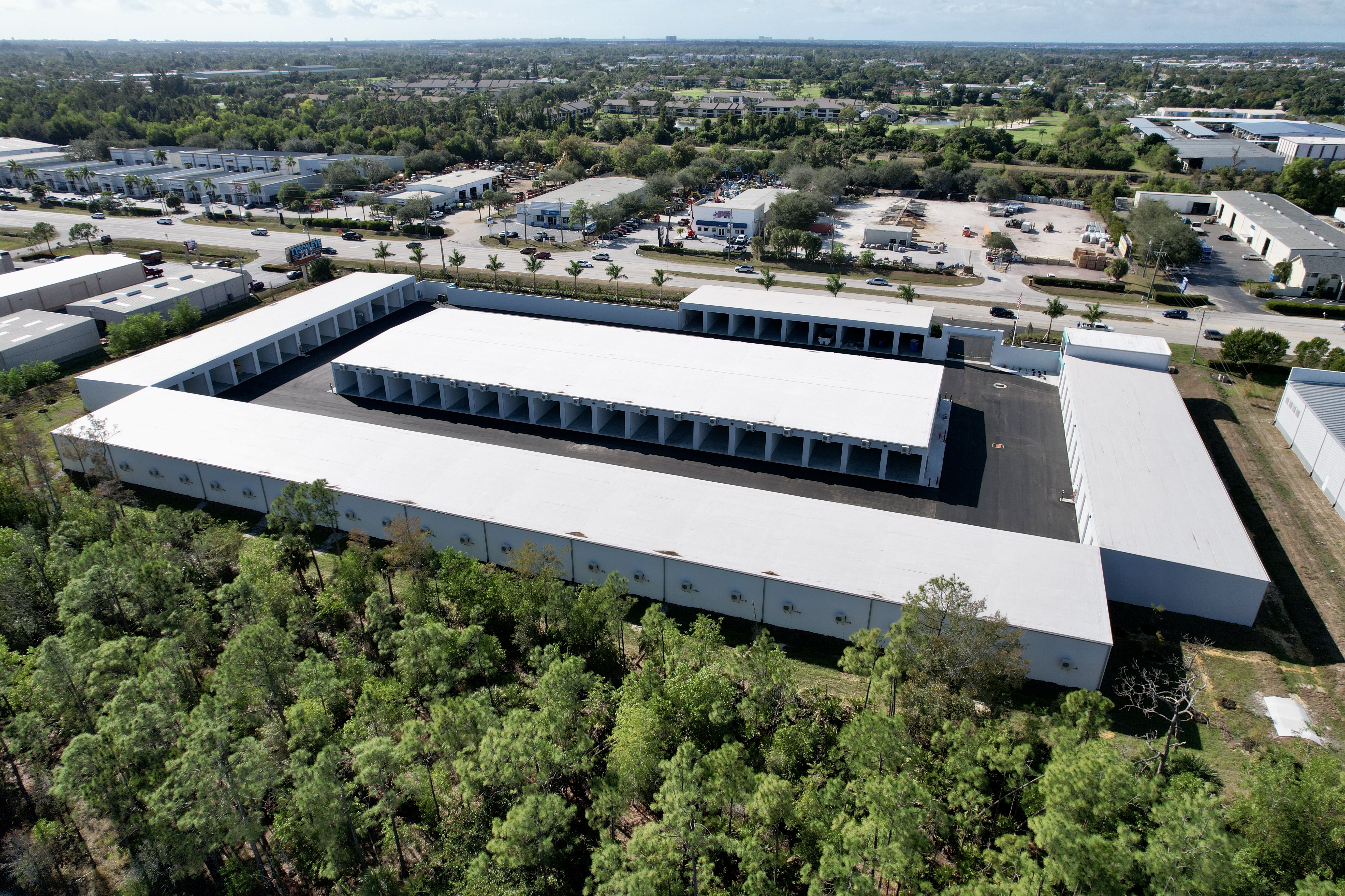 Aerial drone view of Metro-Maxx, a secure, climate-controlled RV and boat storage facility with multiple long storage buildings and wide concrete drive aisles in Fort Myers, Florida