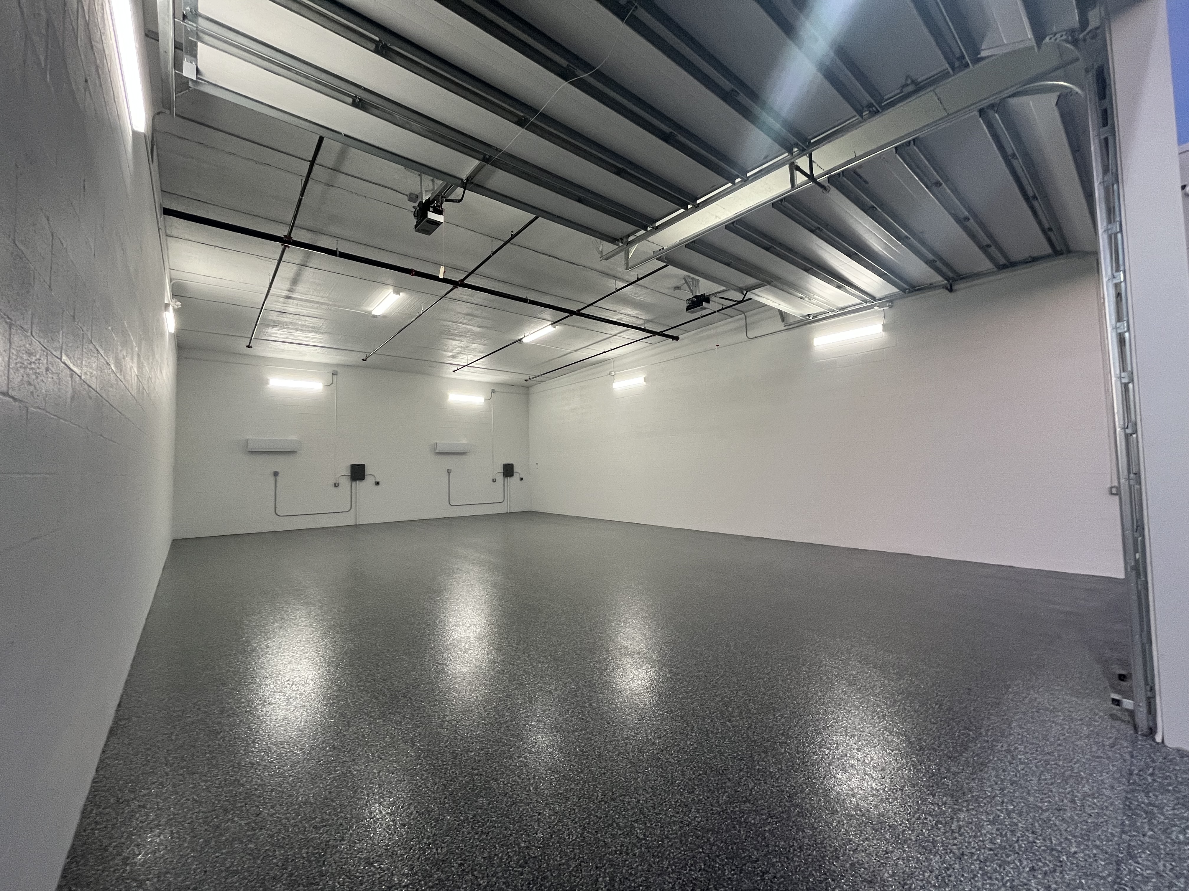 Spacious interior of a double-wide climate-controlled storage unit at MetroMaxx in Fort Myers, featuring white cinder block walls, a polished gray epoxy floor, multiple wall-mounted air conditioning units, bright fluorescent lighting, and a large roll-up door.