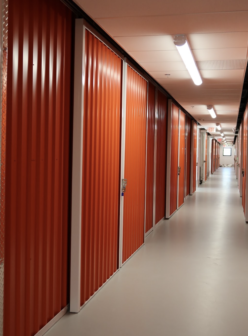 Indoor hallway lined with orange storage unit doors and overhead lighting at Dependable Storage in Prairieville.