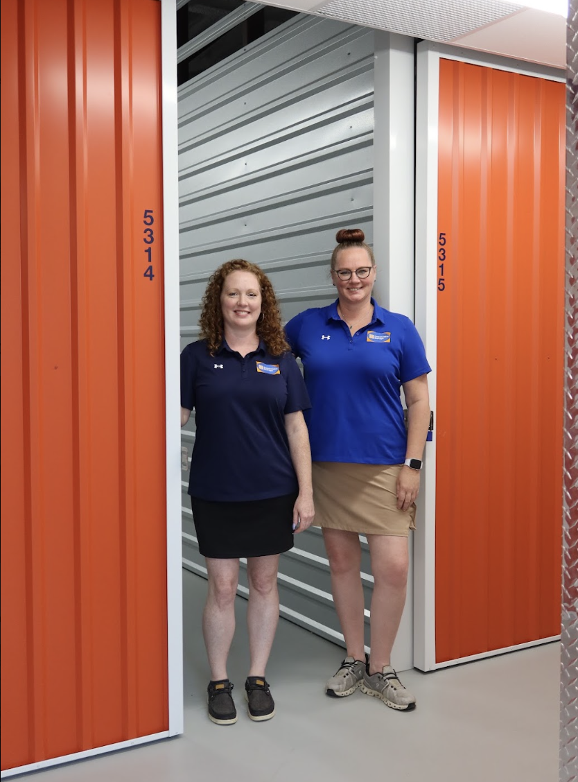 Two Dependable Storage team members in branded blue shirts standing beside indoor storage units at the Prairieville facility.
