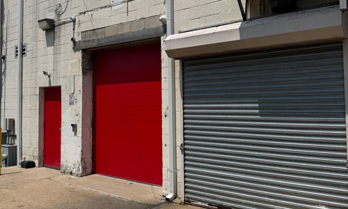 Exterior photo showing a red and grey metal rolling security doors, and a red door to the left.
